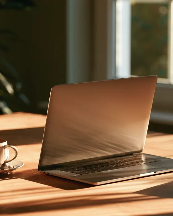 A laptop open on a wooden table in morning light